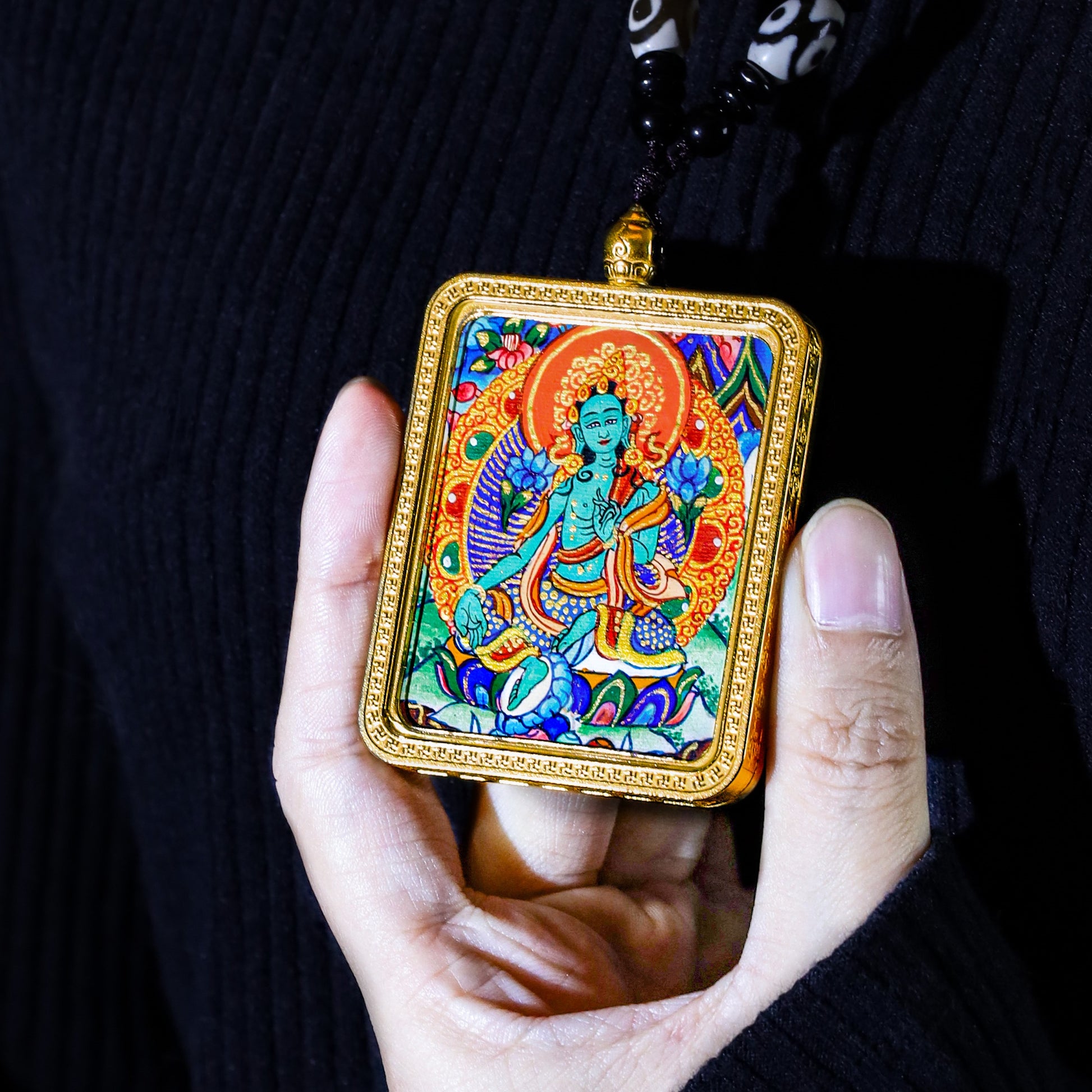 Hand holding a 24K gold hand-painted Green Tara thangka pendant showcasing intricate art and craftsmanship.