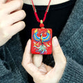 Cinnabar Fire Phoenix Thangka Pendant held by a person, showcasing vibrant colors and intricate design.