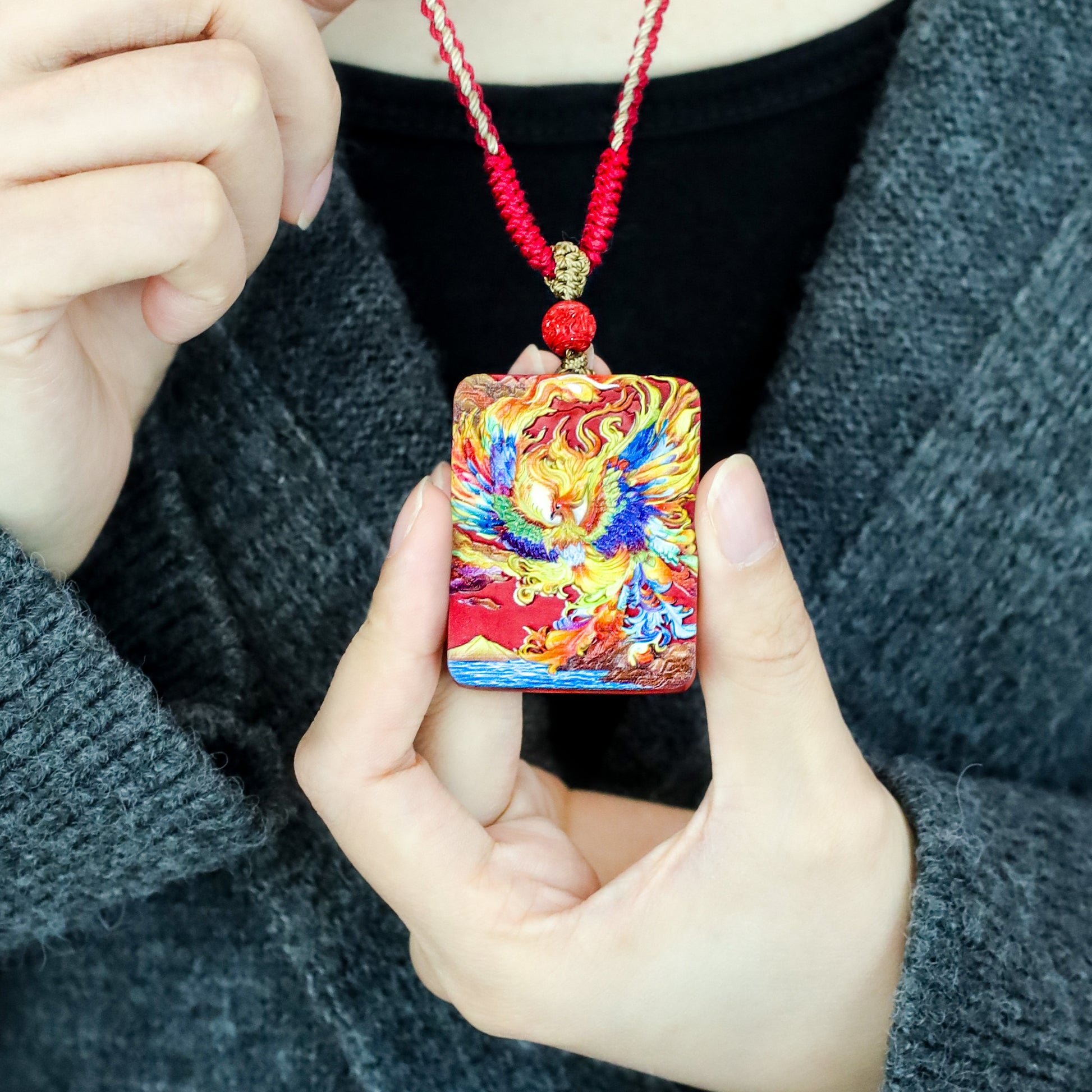 Cinnabar Fire Phoenix Thangka Pendant held in hand, showcasing intricate design and vibrant colors for spiritual style.